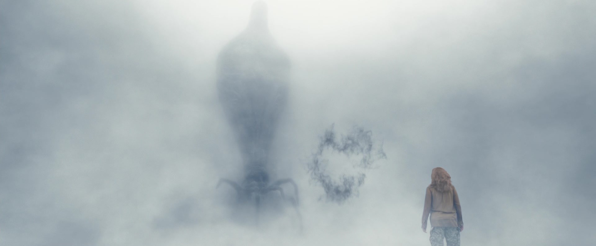 A woman walking through fog toward a massive alien creature, with a ring of dark smoke hanging in the air between them.